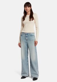 Off-white geribbelde lange mouw top gecombineerd met licht gewassen wijde jeans. De jeans hebben subtiele vervaging en een relaxte pasvorm. Zwarte schoenen maken de look compleet.