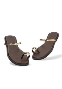 Sandalias planas marrones con suelas negras, que cuentan con un anillo dorado en el dedo del pie y una cinta dorada en la parte superior, mostradas sobre un fondo blanco.