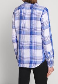 Camicia a quadri blu e bianchi con maniche lunghe, colletto a bottoni e orlo leggermente curvo. Realizzata in tessuto leggero che presenta un motivo testurizzato.