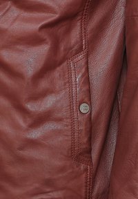 Rote Lederjacke mit glatter Textur, ausgestattet mit einer Seitentasche mit einem silbernen Druckknopf und detaillierten Nähten entlang der Säume.