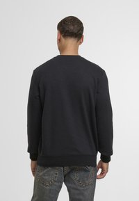 Zwarte crewneck sweater met lange mouwen, ribgebreide boorden en zoom, van achter bekeken. Zachte textuur, eenvoudig ontwerp, geen zichtbare logo's.