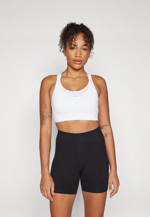 White sports bra with wide straps and a fitted design paired with high-waisted black shorts. Smooth texture, no patterns or hardware.