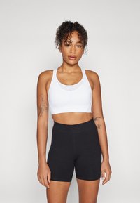 Hvid sports-bh med brede stropper og tætsiddende design, parret med høj talje sorte shorts. Glat tekstur, ingen mønstre eller hardware.