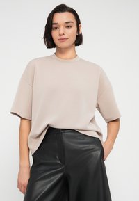 Μπεζ υπερμεγέθη μπλουζάκι με κοντά μανίκια και στρογγυλή λαιμόκοψη, συνδυασμένο με μαύρο δερμάτινο παντελόνι με φαρδιά πόδια. Λεία υφή, casual εφαρμογή.