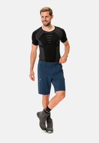 Camiseta atlética de manga corta negra con detalles texturizados, combinada con pantalones cortos azul marino con un bolsillo con cremallera. Botas de senderismo grises y calcetines negros en contraste.