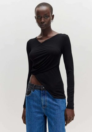 Zwarte blouse met lange mouwen en een wikkeldesign, met een V-hals en een gestructureerde stof, gecombineerd met middelhoge blauwe jeans.