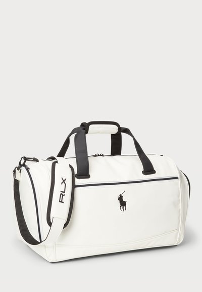 Vit duffelväska med svarta detaljer och logotyp, tillverkad av strukturerat material. Har dubbla handtag, justerbar rem och ficka med dragkedja.