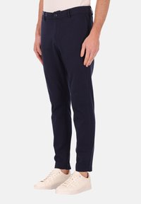 Marineblauwe op maat gemaakte broeken van rekbare stof, met een platte voorkant, riemlussen en zijzakken, gecombineerd met witte sneakers.