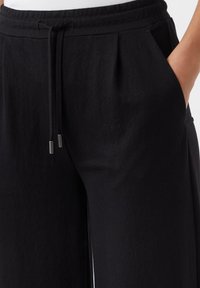 Black wide-leg pants made of soft fabric, featuring a drawstring waistband, side pockets, and subtle pleats for added detail.