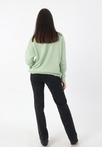Hellgrüner, übergroßer Pullover mit geripptem Saum, kombiniert mit schwarzen, geraden Jeans. Weicher Stoff, lockere Passform und minimale Details.