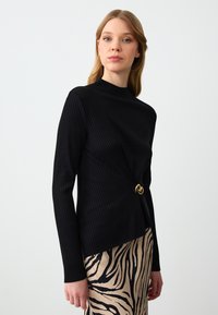 Zwarte geribde langemouwen top met een hoge hals en gouden ronde hardwareaccent, gecombineerd met een patroonrok met een zebraprint.