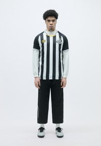 Svart og hvitstripete genser med rund hals og lange hvite ermer, paret med svarte bukser med sidesømmer; svarte sko.