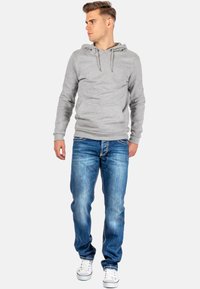 Grijze katoenen hoodie met een trekkoordkap, gecombineerd met blauwe denim jeans met een vervaagd uiterlijk. Witte sneakers maken de outfit compleet.