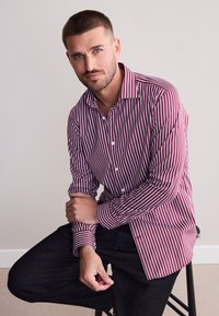 Rot-weiß gestreiftes langärmeliges Hemd zum Knöpfen, mit einem Kragen und Manschetten, kombiniert mit schwarzen Hosen. Glatte Stoffstruktur.