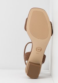 Sandale à talon marron tissée avec un dos ouvert, une semelle texturée et un talon carré, présentant un design minimaliste et un matériau synthétique.