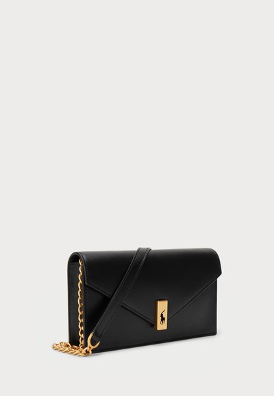 Clutch de cuero negro con diseño plegable, herrajes dorados y una correa de cadena. Presenta un detalle de logo dorado en la parte frontal.