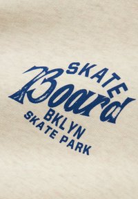 Tessuto di cotone crema con stampa serigrafica blu: "SKATE Board BKLYN SKATE PARK" dallo stile vintage e dall'aspetto leggermente usurato.