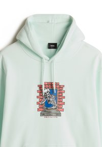 Mintgrüner Kapuzenpullover aus weichem Stoff. Verfügt über einen grafischen Druck eines Skeletts in einem Fenster mit Ziegelakzenten und Text darunter.