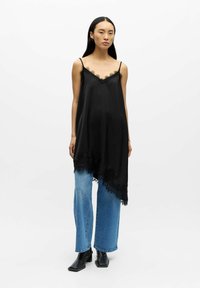 Svart silkeaktig kjole med blonderkant og justerbare stropper, asymmetrisk falme, kombinert med vide blå denimbukser og svarte ankelstøvler.