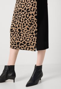 Gonna a stampa leopardata con pannello laterale nero, caratterizzata da una texture liscia. Stivaletti neri alla caviglia con punta affusolata e dettagli con zip.