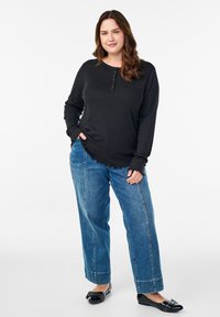 Musthave mustrikiga long-sleeve henley, mille on nupud ja lokkis äär, kombineeritud hästivoolavate siniste teksade ja mustade madalate kingadega.