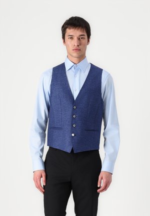 Marineblå vest med teksturert stoff, featuring fem knapper, to frontlommer og en figurnær design, brukt over en lyseblå skjorte.