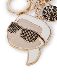 Gold-tone keychain featuring a stylized face with black sunglasses, a beige background, and white accents, made of glossy material.