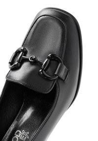 Chaussure en cuir noir avec un bout carré, dotée d'une boucle noire proéminente sur le devant et d'une semelle intérieure texturée.