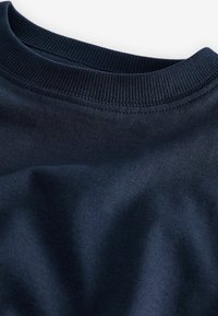 Námořnická modrá mikina s žebrovaným výstřihem. Materiál je hladký a mírně texturovaný, vykazuje jemné záhyby a stíny v látce.
