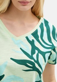 V-kauluspaita vaaleanvihreänä, jossa on teal- ja sinisiä abstrakteja lehtikuvioita, valmistettu pehmeästä, kevyestä kankaasta, jossa on sileä pinta.