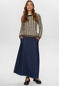 Strickpullover mit Karomuster in Beige und Braun, kombiniert mit einem Jeans-Maxikleid. Der Rock verfügt über seitliche Taschen und Kontrastnähte.