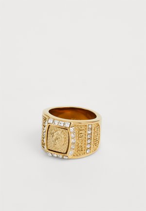 Gold-tone ring with a textured rectangular face, featuring a central emblem and surrounded by clear rhinestones on the band.