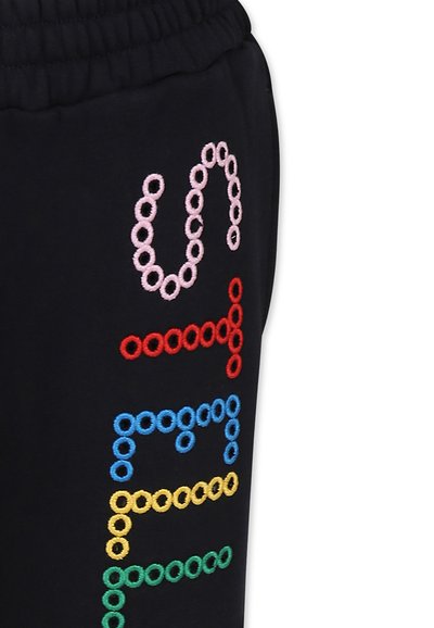 Pantaloni della tuta neri con lettere ricamate multicolori in rosa, rosso, blu, giallo e verde disposte in un motivo circolare lungo la gamba.