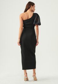 Black, form-fitting midi dress with one shoulder design. Features a textured fabric and sheer puff sleeve on the left side.