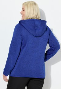 Felpa con cappuccio blu, strutturata, con cappuccio foderato, maniche lunghe e vestibilità comoda. Le macchie più scure creano un contrasto con il tessuto blu vivace.