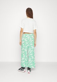 Zkrácený bílý tričko s krátkým rukávem, doplněné mátově zelenými kalhotami s širokými nohavicemi, které mají bílý květinový vzor. Celý vzhled doplňují černé tenisky.