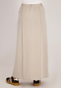 Beige maxi rok met een gladde textuur, een elastische tailleband en zijsplitten. Gecombineerd met bruine sneakers met witte strepen.