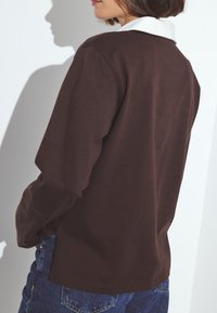 Ruda ilgomis rankovėmis marškiniai su baltu apykakle, pagaminti iš minkštos medžiagos. Turintys laisvą siluetą ir matomus siuvinėjimo elementus.