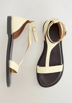 Gule lædersandaler med et minimalistisk design, der har flade såler, justerbare ankelremme og en glat overflade. Ingen synlige mønstre.