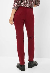 Pantalons ajustés bordeaux avec une texture lisse, dotés de poches arrière, portés avec des bottes noires à semelles chunky, montrés de côté.