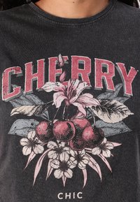Mustahuone T-paita, jossa on graafinen printti kirsikoista, kukista ja sanasta "CHERRY" paksulla, kuluneella punaisella kirjainmuodolla.