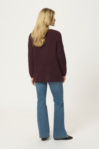 Bordeauxfarbener, strukturierter Strickpullover mit langen Ärmeln, lockerer Passform und einem etwas längeren Rückensaum, kombiniert mit hellblauen Schlagjeans.