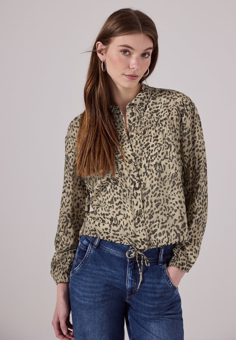 Leopard-print button-up shirt in beige and black, lightweight fabric, long sleeves with elastic cuffs, tied waist, paired with blue jeans.