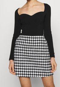 Svart ribbad långärmad topp med en hjärtformad halsringning, kombinerad med en svart och vit rutmönstrad kjol med en texturerad yta.