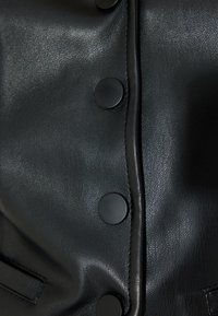 Textur des schwarzen Lederjackets mit einer auffälligen Reihe großer schwarzer Knöpfe und dezenten Nähdetails, die ein glattes, weiches Finish aufweisen.