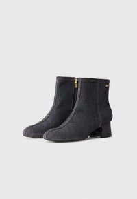 Botas de tornozelo de ganga escura com fecho lateral, bico apontado e salto médio. Costura em contraste e detalhe do logótipo na lateral.