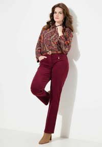 Pantaloni di velluto a coste color bordeaux con taglio dritto, abbinati a una blusa a maniche lunghe con motivo e una cintura marrone, completati da stivaletti beige con tacco.