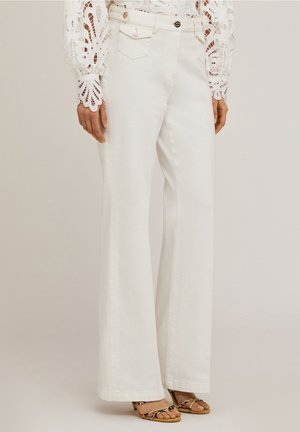 Witte broek met brede pijpen, voorzakken met klep en knoopdetails, gecombineerd met een top met kanten mouwen en sandalen met gevlochten bandjes op een lichte achtergrond.