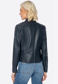 Giacca di pelle blu scuro con design aderente, cuciture visibili e lunghezza corta, caratterizzata da un colletto alto e una texture liscia.