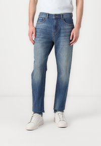 Dark blue denim jeans with a straight leg design, featuring five pockets and a slight fade, paired with white sneakers.